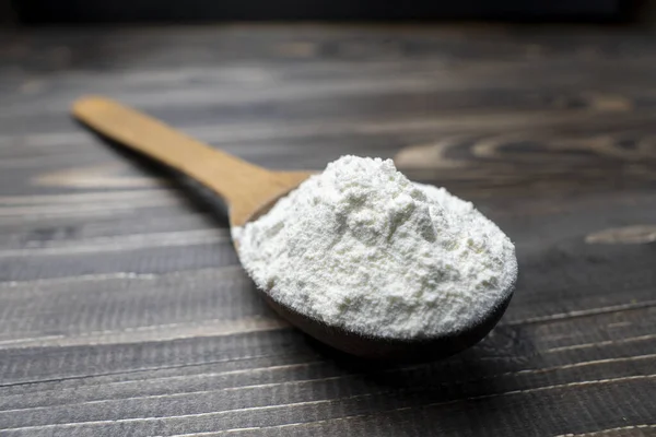 Koyu renkli ahşap arka planda kaşıkla un. Manzarayı kapat. Ev yapımı pişirme hazırlıkları. Pişirmek için temel malzemeler. Tahta kaşıkta buğday unu. 