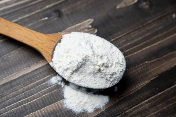 Koyu renkli ahşap arka planda kaşıkla un. Manzarayı kapat. Ev yapımı pişirme hazırlıkları. Pişirmek için temel malzemeler. Tahta kaşıkta buğday unu. 