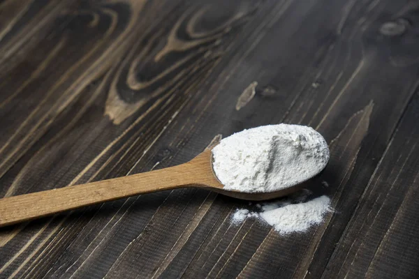 Koyu renkli ahşap arka planda kaşıkla un. Manzarayı kapat. Ev yapımı pişirme hazırlıkları. Pişirmek için temel malzemeler. Tahta kaşıkta buğday unu. 