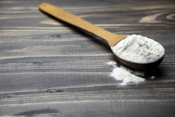 Koyu renkli ahşap arka planda kaşıkla un. Manzarayı kapat. Ev yapımı pişirme hazırlıkları. Pişirmek için temel malzemeler. Tahta kaşıkta buğday unu. 