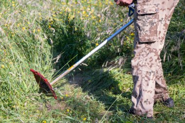 Koruyucu maskeli olgun bir adam bahçede çimleri buduyor.