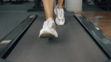 Koşu bandı ve ayak. Spor salonunda kardiyo çalışması yapan atletik bir kadının düşük açılı görüntüsü. Kusursuz döngü