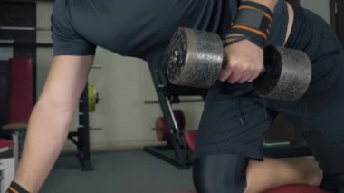 Elinde dambıl olan vücut geliştirici spor salonunda güç antrenmanı yapıyor. El kamerasıyla yakın çekim.
