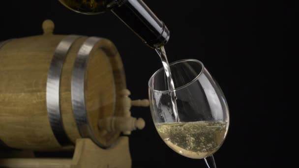 酒从瓶子里倒入杯子里 白葡萄酒洒在酒杯中 背景为橡木老化桶 — 图库视频影像