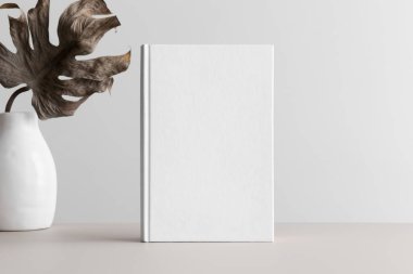 Beyaz kitap, bej bir masadaki vazoda canavar yaprağı olan bir maket..
