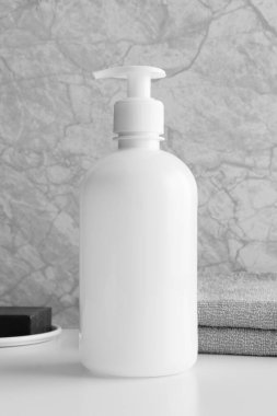Beyaz kozmetik sıvısı sabun şişesi, beyaz masanın üzerinde sabun ve havlu var..