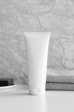 Beyaz masasında beyaz bir havlu ve sabun bulunan beyaz bir krem tüpü..