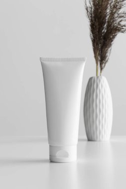 Beyaz masadaki beyaz çiçekli beyaz krema tüpü..