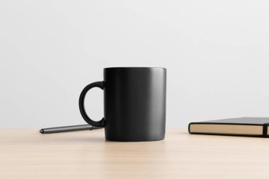 Ahşap masada çalışma alanı aksesuarları olan siyah kupa modeli..