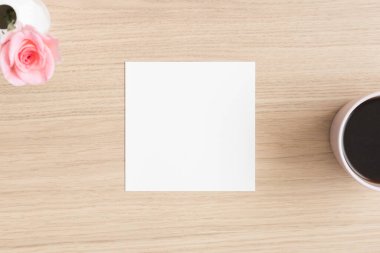 Kare davetiye maketi, üzerinde gül ve bir fincan kahve olan ahşap masa..