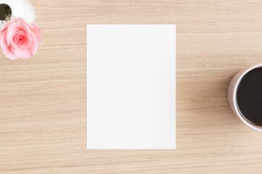 Beyaz davetiye maketi, üzerinde gül ve bir fincan kahve olan tahta masa. 5x7 oranı, A6, A5 'e benziyor..