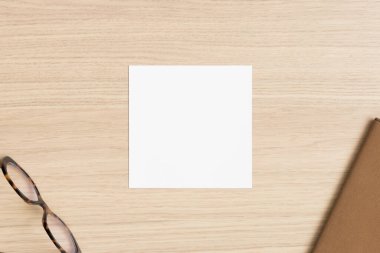 Ahşap masanın üzerinde cam ve çalışma alanı aksesuarları olan kare davet kartı modeli.