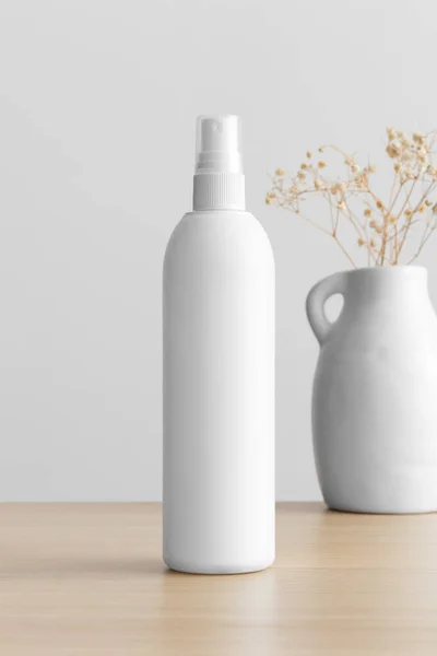 White cosmetic spray bottle mockup with a gypsophila on the wooden table.