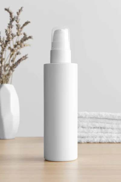 White cosmetic lotion bottle mockup with a lavender and towels on the wooden table.