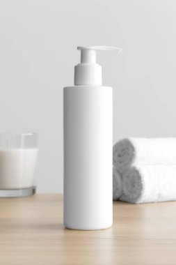 Beyaz kozmetik şampuan şişesi. Ahşap masanın üzerinde mum ve havlular var..