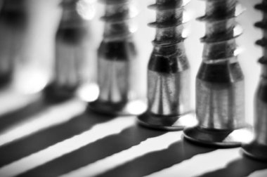 Vidalar beyaz masanın üstünde dikey olarak duruyor. Siyah ve beyaz uzun gölgeler bırakıyorlar.