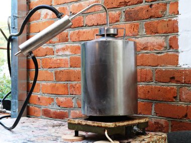 Moonshine hala eski bir ısıtma tabağında, tuğla bir duvarın arkasında duruyor. Evde alkol üretimi, damıtma ekipmanları, kırsal alanda ev damıtıcısı.