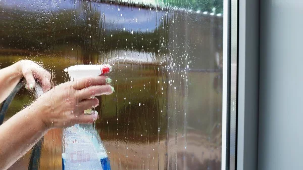 window cleaning with a chemical spray by women from the street side, glass washer visible through drops and smudges on a transparent surface, house cleaning by a housewife
