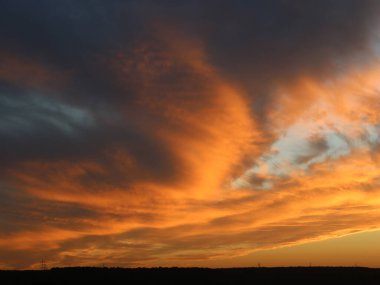 Günbatımında turuncu-gri gök gürültülü bulutlar karanlık bir orman şeridi üzerinde dramatik bir manzara engin ve fırtınalı bir gökyüzü, akşam vakti gökyüzünde gök gürültülü bulutlar.