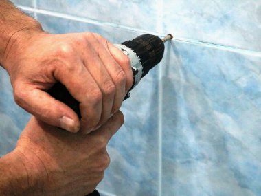 Seramik kiremitlerin arasındaki bir duvarda seramik bir duvarda delik açmak, erkek eli zorla bir duvarı delmek.