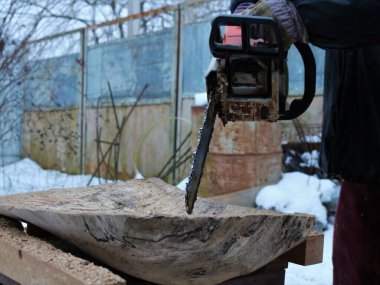 Kışın kırsal bir alanda, bir marangoz tarafından ahşap dokulu katı bir katman işlemek, ahşap işleme aracıyla katı ahşaptan dekoratif nesneler yaratmak, bir odun parçasına oyuk açmak,