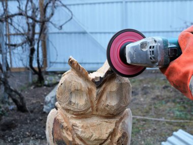 Öğütücüde öğütücü bir disk kullanarak ahşap bir baykuş heykeli kullanarak ahşap bir dekor oluşturma sürecinde ahşap bir ürünün yüzeyini işlemek