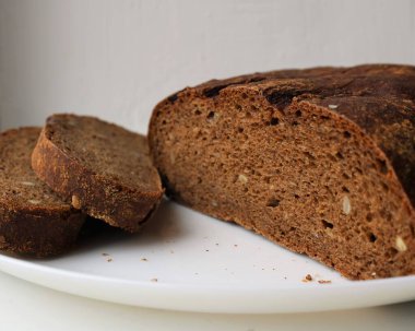 Çavdar ekmeği ekmeği, tahıl ve tohumla karıştırılmış fırınlanmış hamur desenli bir bölümde. Diyet için sağlıklı ekmek, beyaz bir tabakta dilimlenmiş.