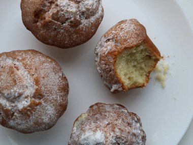 Beyaz bir tabakta pudra şekerli dört kahverengi çöreğin üst görüntüsü yemek dokusu arka planında, tatlı hamur tatlısı şekerli çöreklerle yatıyordu. Biri büyük beyaz bir tabakta ısırılarak koparılmıştı.
