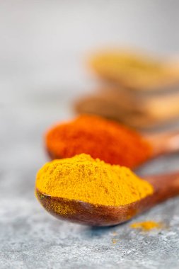 Arkasında başka baharatlar olan kaşık üzerinde canlı zerdeçal tozu yakın plan.