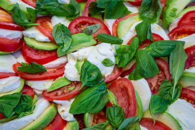 A summer salad of tomato, mozzarella, avocado and basil leaves
