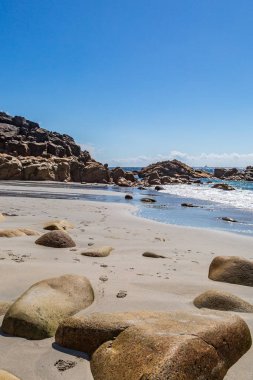 Rock formations on Porth Nanven beach at low tide, with a blue sky overhead