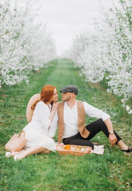 Piknik. Bahar çayırında sevimli bir çift. Çiçek açan kiraz ağaçları sokağı. Eski tarz. Meyve sepeti, hasır şapka.