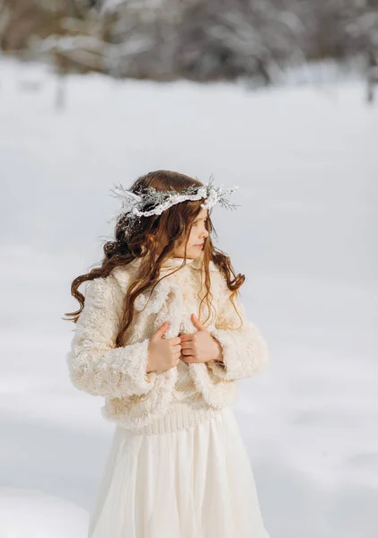 快乐的卷曲的小女孩 戴着花环 穿着一件雪白的外套 在冬日的公园里 站在雪地里 扔着雪 阳光灿烂的日子 圣诞节 — 图库照片