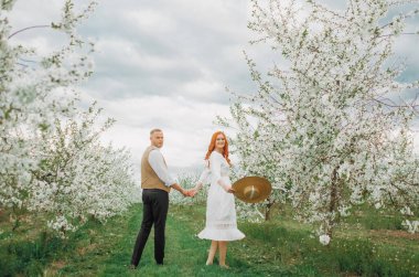 Açık havada aşık mutlu bir çift. Sevgi dolu bir adam ve kadın bahar çiçekli bir parkta yürüyorlar..