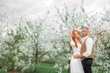 Beyaz çiçeklerin arka planında kucaklaşan sevgi dolu bir çift. Eski tarz, hasır şapkalı kız..