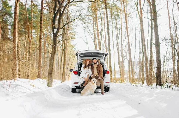 Bej renkli köpekli gülümseyen çift karlı ormanda açık bir arazi aracının bagajında oturuyor. Aktif kış tatillerinde birbirimizin keyfini çıkarıyoruz..