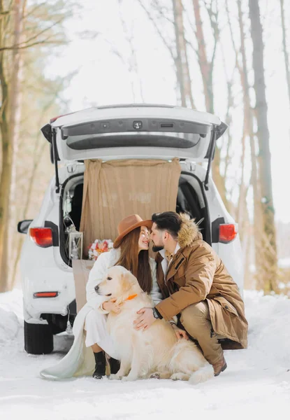 Bej renkli köpekli gülümseyen çift karlı ormanda açık bir arazi aracının bagajında oturuyor. Aktif kış tatillerinde birbirimizin keyfini çıkarıyoruz..