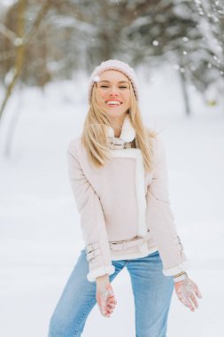 Pembe paltolu ve şapkalı mutlu kadın kış parkında yürüyor.