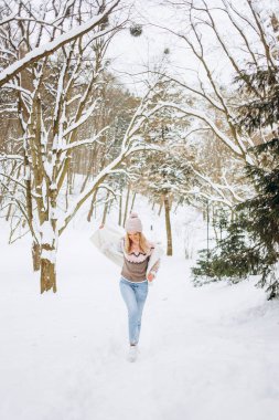 Pembe paltolu ve şapkalı mutlu kadın parkta kış yolunda koşuyor. Eğlence konsepti, kış zamanı..