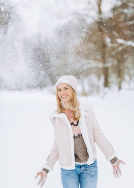 Mutlu komik sarışın kadın soğuk mevsimin keyfini çıkarmak için ellerini havaya kaldırarak kar fırlatıyor.