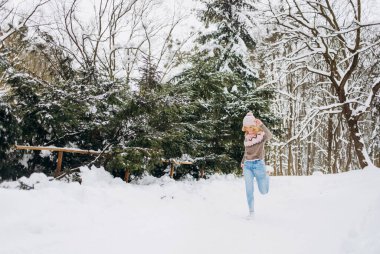 Pembe paltolu ve şapkalı mutlu kadın parkta kış yolunda koşuyor. Eğlence konsepti, kış zamanı..