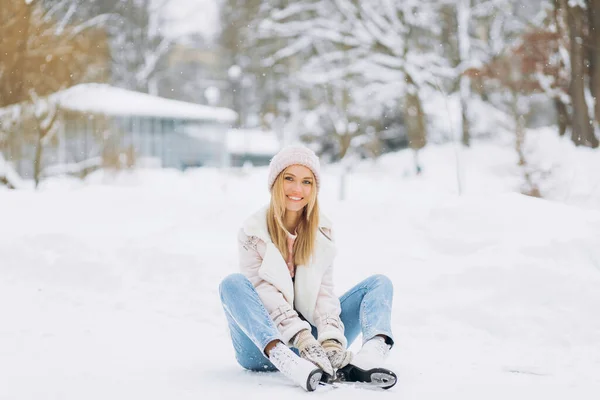 一位漂亮的女士穿着冰鞋坐在冬日公园里结冰的雪地上 — 图库照片