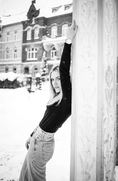 穿着黑色毛衣和牛仔裤的年轻女子在冬日街上摆出一副黑白照片 — 图库照片