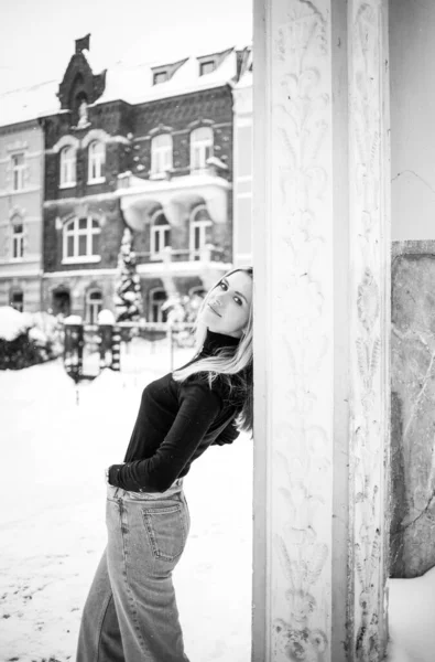 穿着黑色毛衣和牛仔裤的年轻女子在冬日街上摆出一副黑白照片 — 图库照片