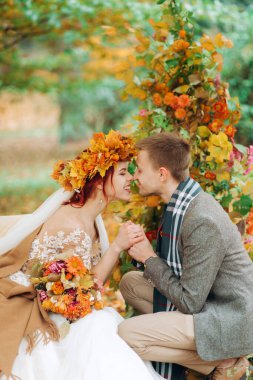 Güzel yeni evliler parkta düğün kemerinin altında oturmuş, birbirlerinin ellerini tutuyorlar..