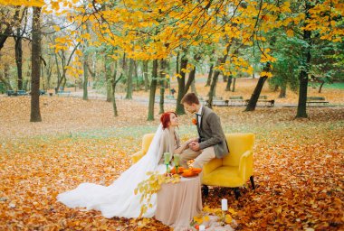 Sonbahar parkında yumuşak sandalyelerde oturan yeni evliler.