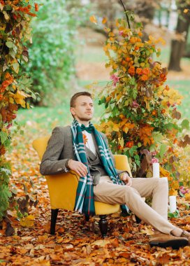 Şık takım elbiseli ciddi bir damat kemerin altında rahat bir sandalyede oturuyor..