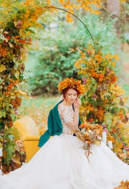 Sonbahar çelengi giymiş gelin parkta rahat bir sandalyede oturuyor.