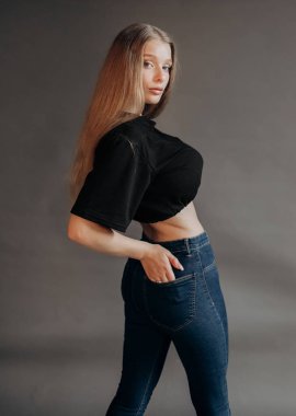 Siyah bluzlu güzel sarışın ve gri arka planda stüdyoda poz veren kot pantolonlu.