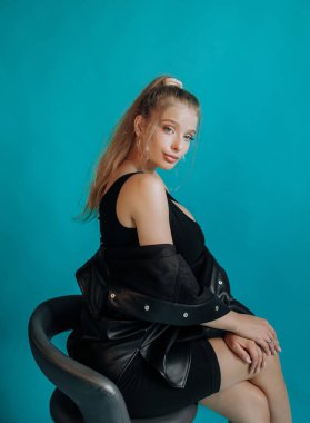 Stüdyoda bir bar taburesinde oturan muhteşem sarışın. Turkuaz arkaplan.